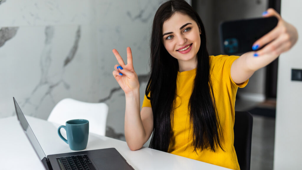 Pretty happy young woman sitting at a table at home with her laptop